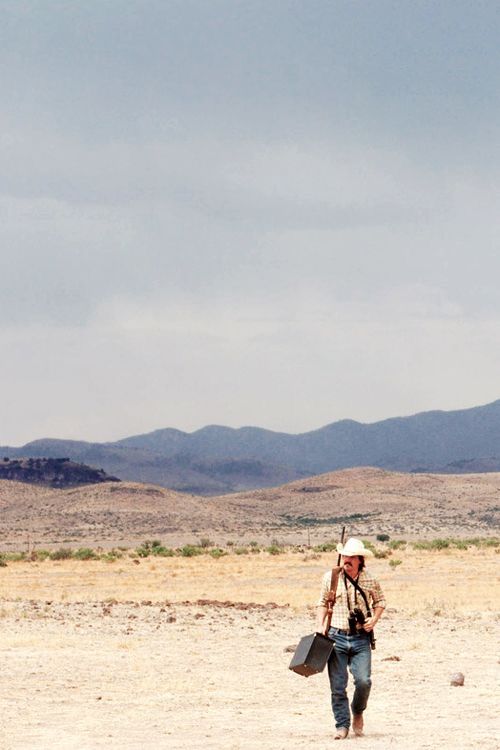 a man walking across a dirt field with a kite in the air