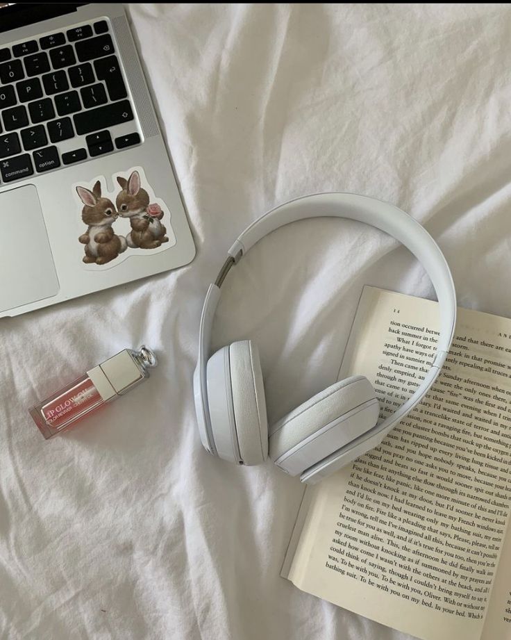 an open laptop computer sitting on top of a bed next to headphones and a book