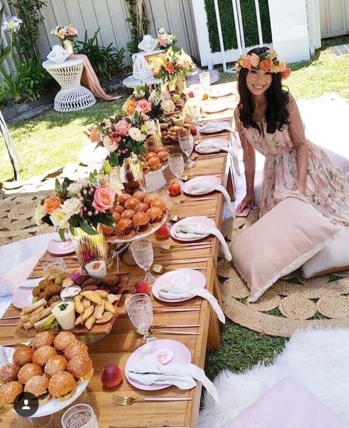 a woman sitting on the ground next to a table filled with plates and bowls full of food