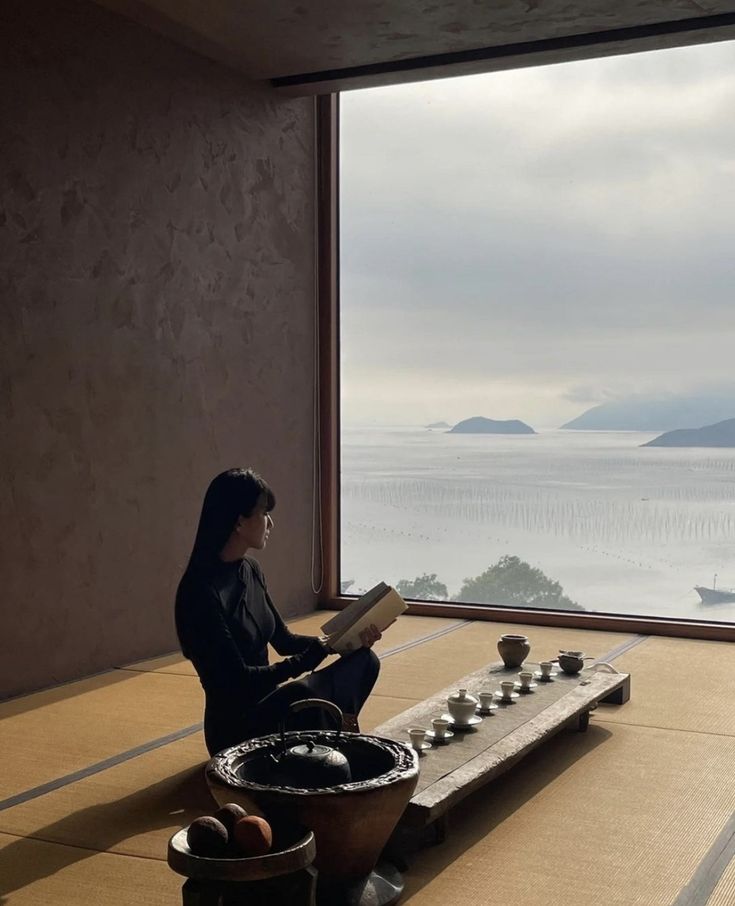 a woman sitting on top of a wooden floor next to a window with an ocean view