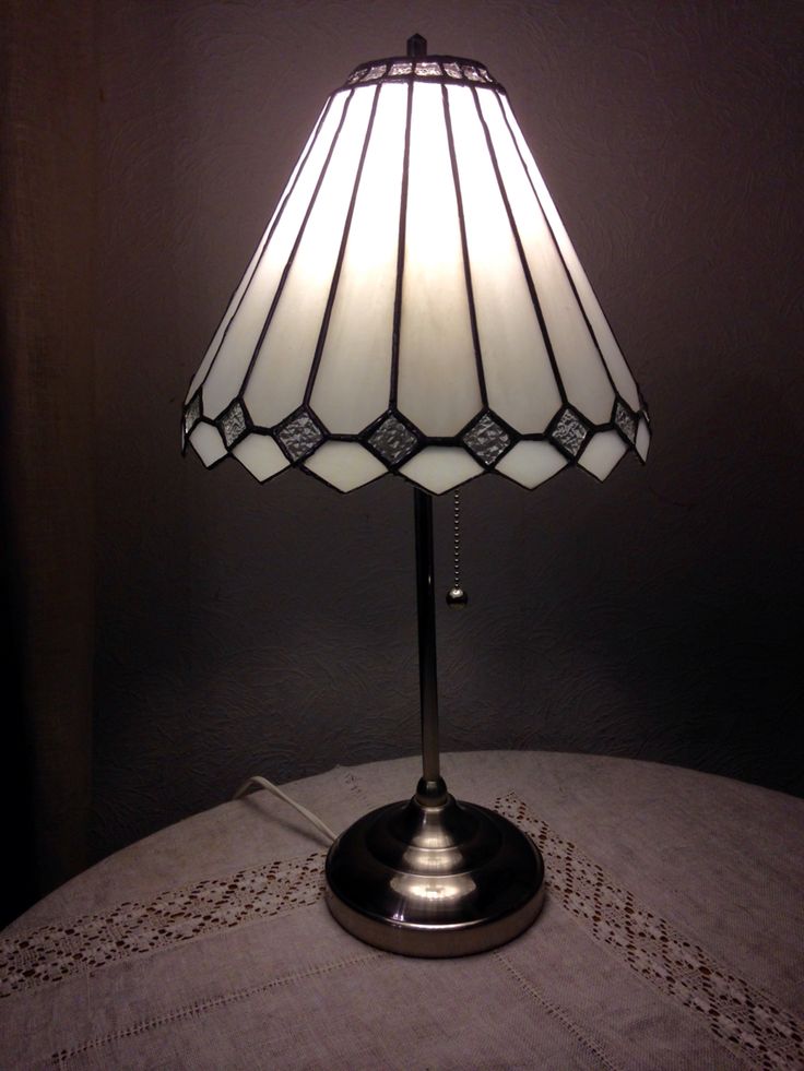 a table lamp sitting on top of a bed next to a curtained window sill