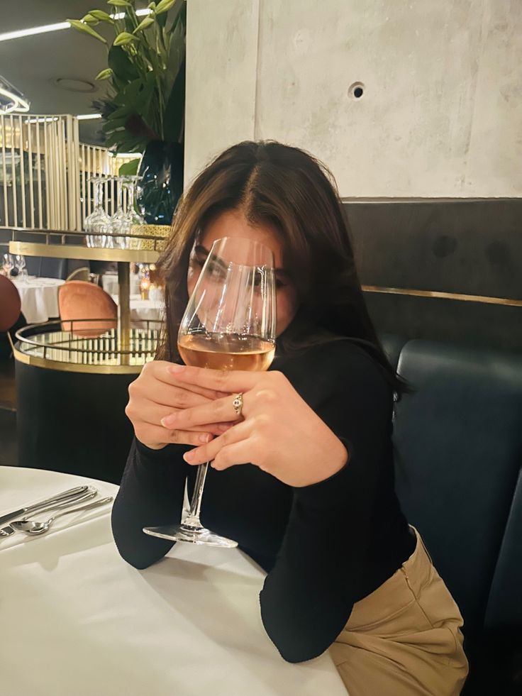 a woman sitting at a table with a glass of wine in front of her face