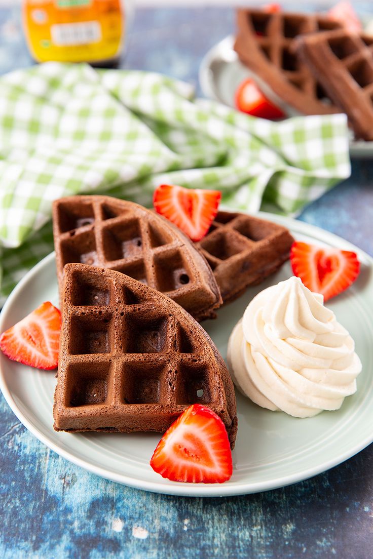 two waffles on a plate with whipped cream and strawberries next to them