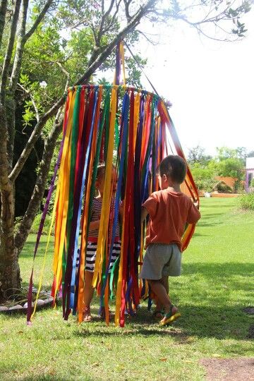 two young boys standing next to each other near a tree with ribbons hanging from it