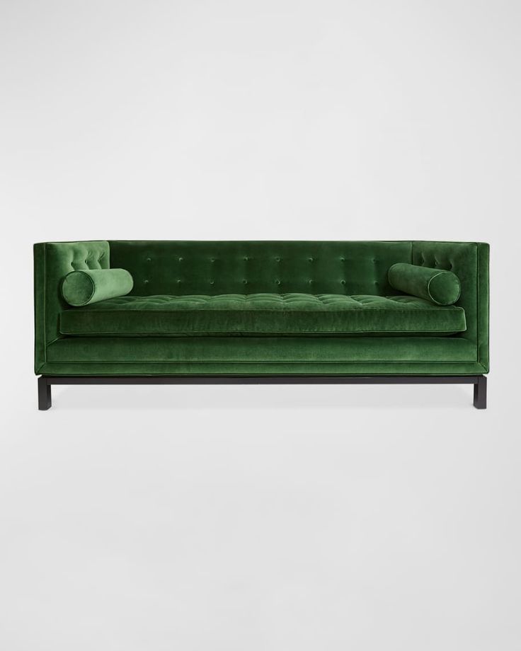 a green velvet sofa with two pillows on it