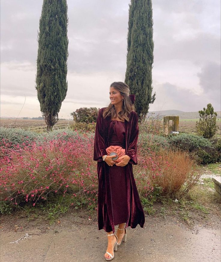 a woman standing in front of some trees wearing a long dress and sandals with her hands on her hips