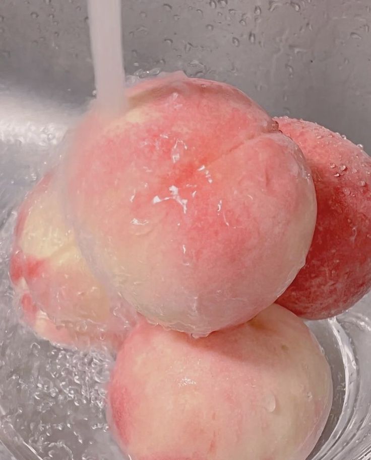 two peaches are being washed in a silver sink with water droplets on it and one is pink