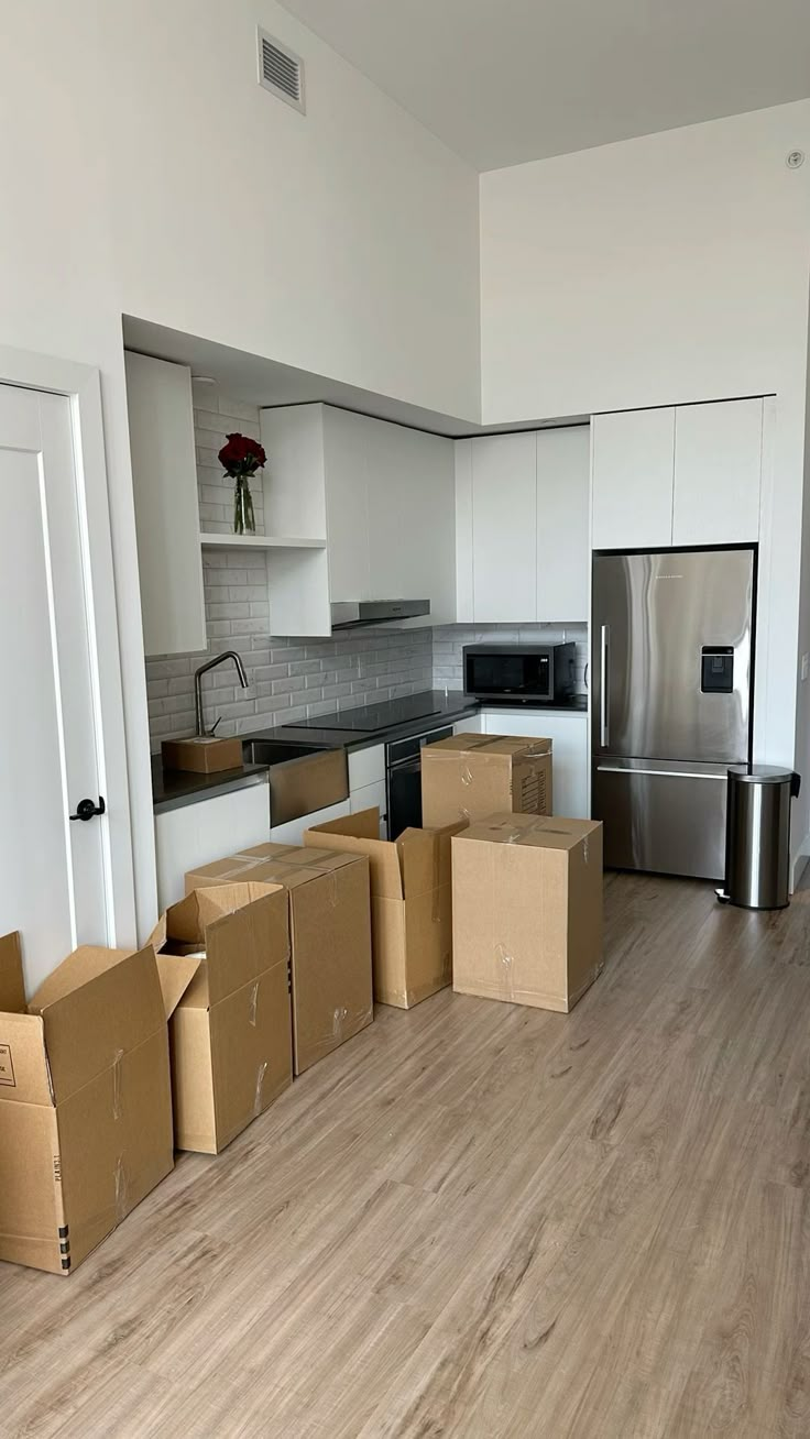 several boxes are stacked on the floor in an empty kitchen with stainless steel appliances and refrigerator