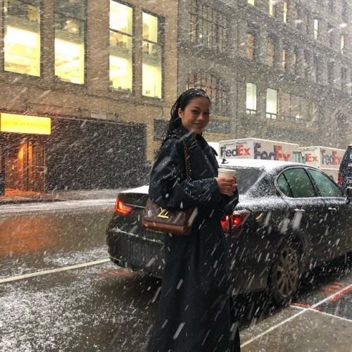 a woman walking down the street in the snow with her handbag on her hip