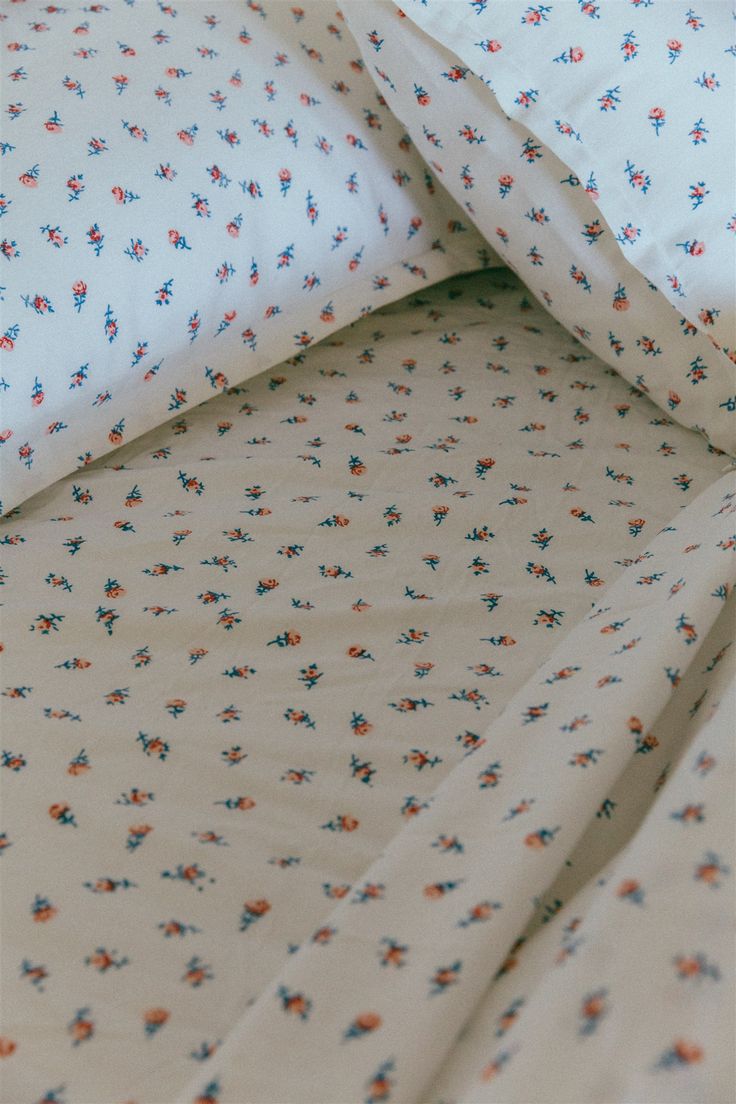 an unmade bed with white sheets and blue and orange flowers on it's edges