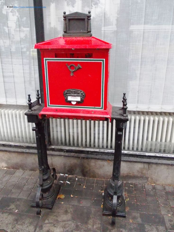 a red and black mailbox sitting on top of a sidewalk next to a building