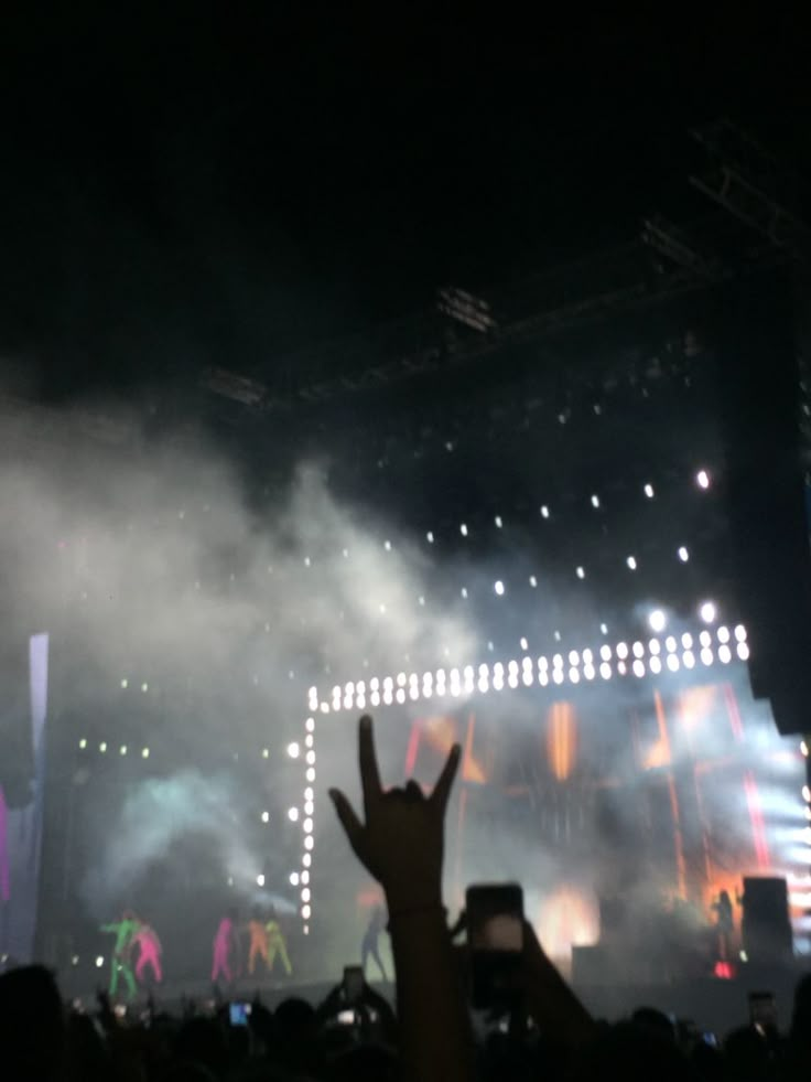 the crowd is watching an outdoor concert with their hands in the air and lights on