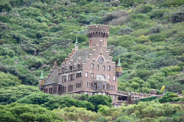 an old building sitting on top of a lush green hillside next to a forest filled mountain