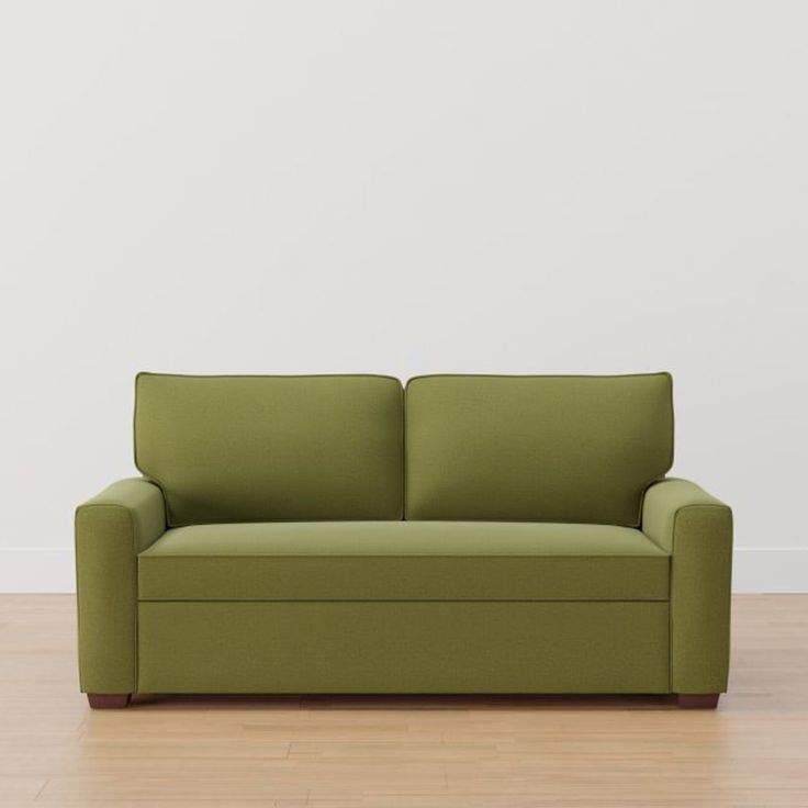 a green couch sitting on top of a hard wood floor next to a white wall