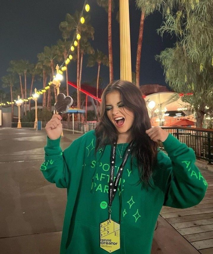 a woman in a green hoodie holding up a cell phone