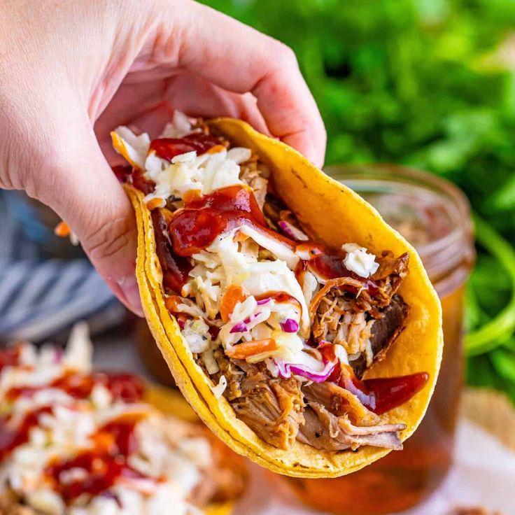 a hand holding up a taco with shredded meat and sauce on it next to other food