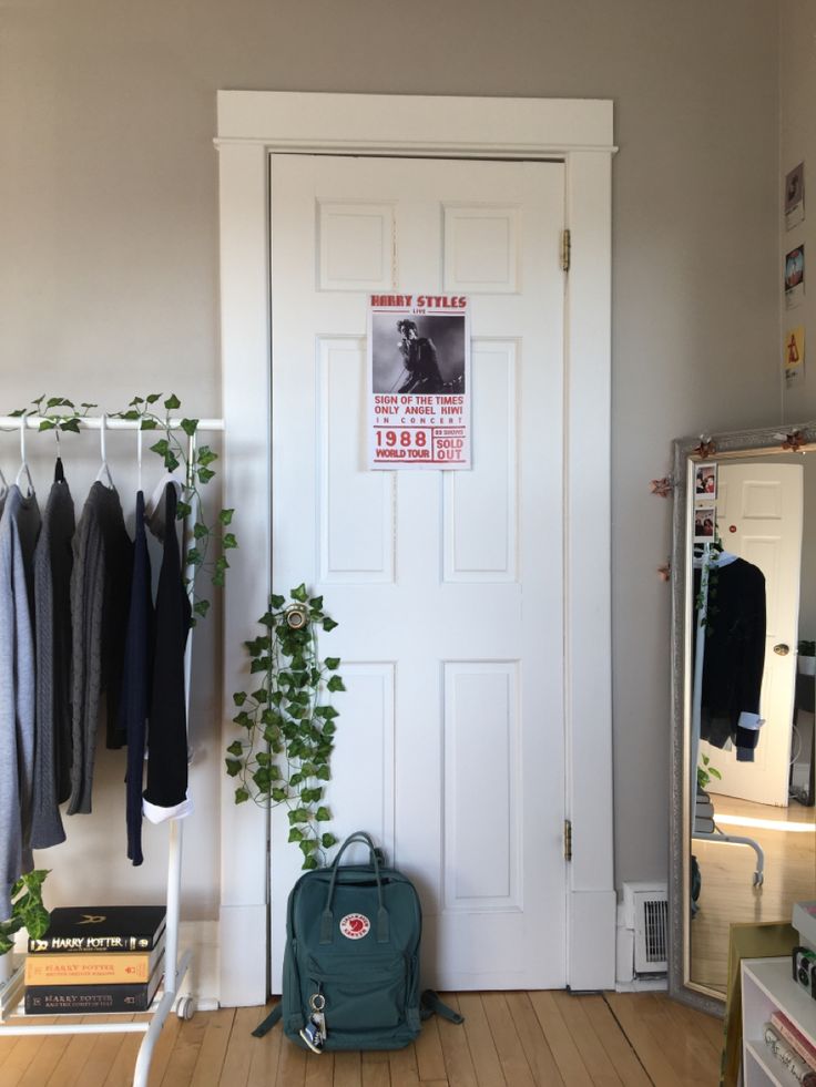 a white door in a room with clothes hanging on the wall and a green backpack next to it