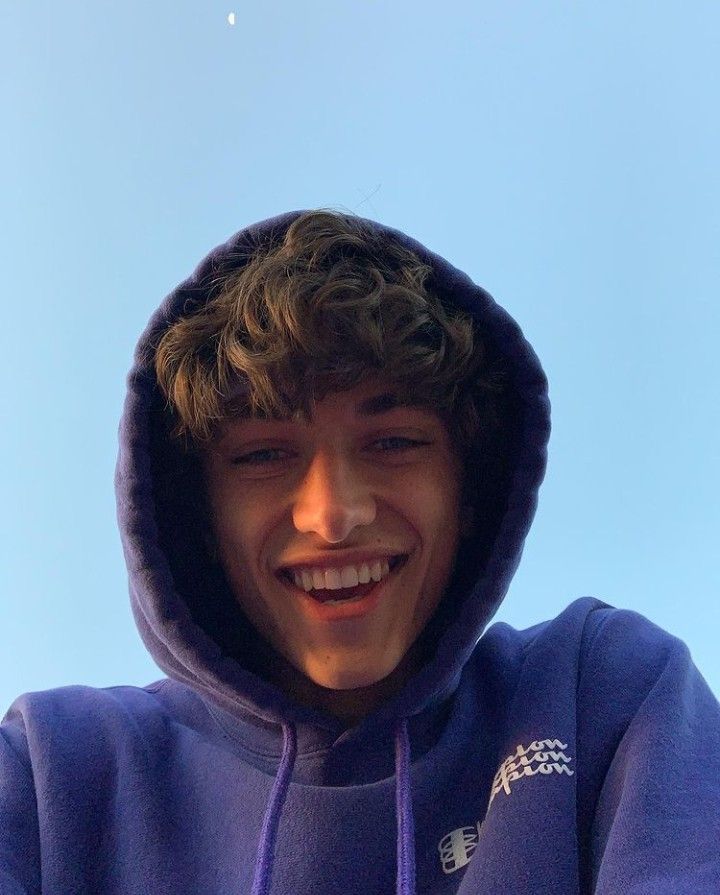 a young man in a blue hoodie smiles at the camera