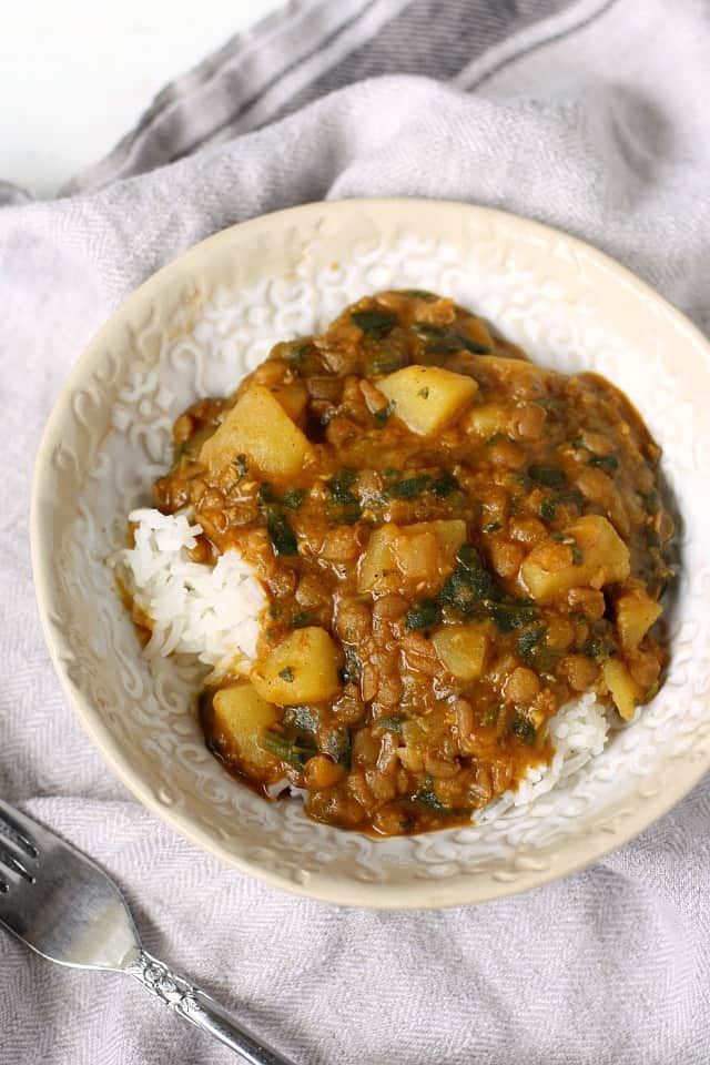 a white bowl filled with stew and rice on top of a gray cloth next to a fork