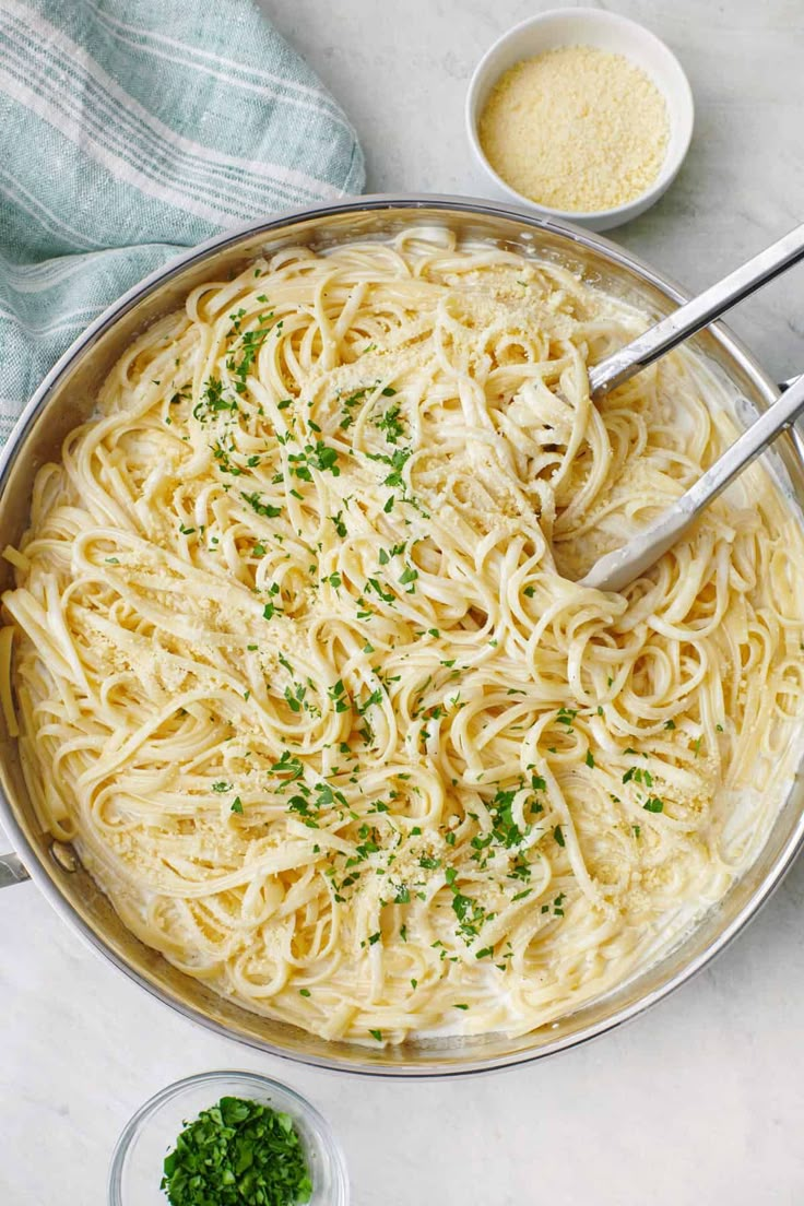 a pan filled with pasta and parsley on top of a white counter next to two bowls