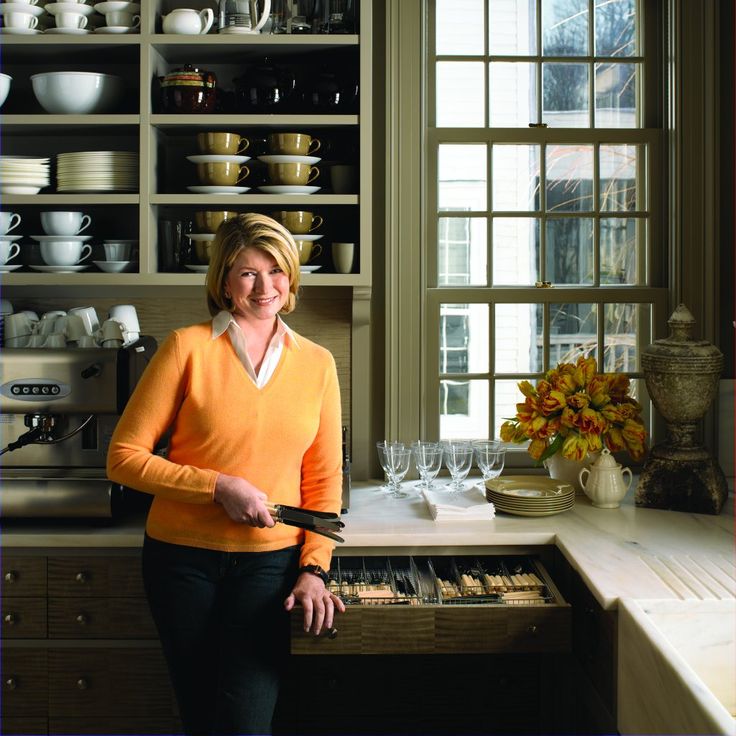 a woman is standing in the middle of a kitchen with dishes on shelving behind her