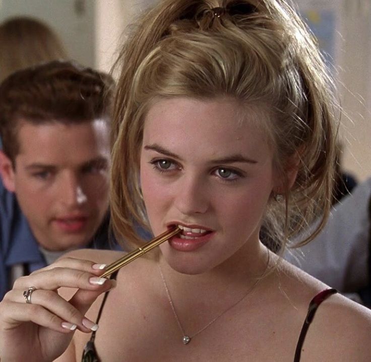 a woman brushing her teeth in front of a mirror with another man behind her looking on