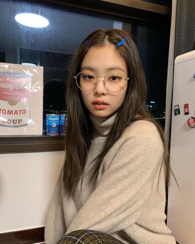 a young woman wearing glasses sitting in front of a refrigerator