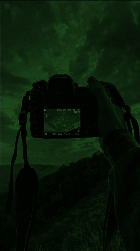 a person holding up a camera to take a photo in the dark with green light