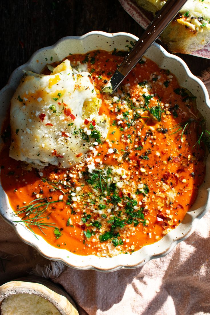 a white bowl filled with food on top of a table next to bread and utensils