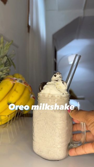 a person holding a glass with ice cream in it and bananas on the table next to it