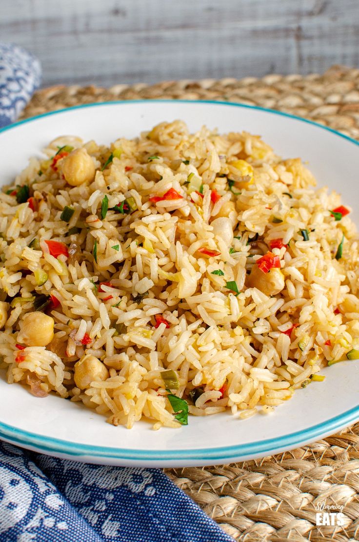 a white plate topped with rice and veggies on top of a woven table cloth