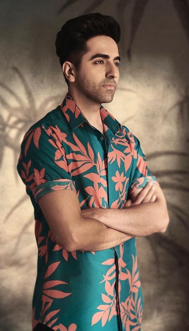 a man with his arms crossed standing in front of a wall wearing a hawaiian shirt