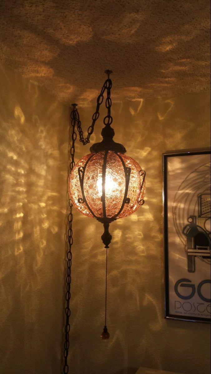 a lamp hanging from the ceiling next to a framed photograph on a wall with light reflecting off it's side