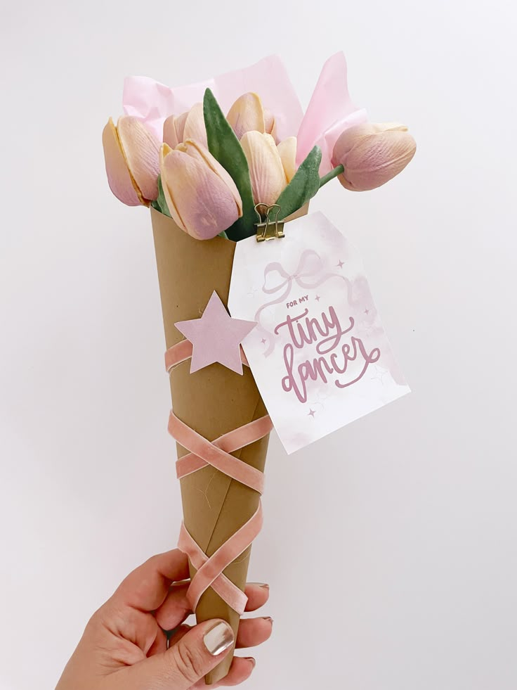 a hand holding a paper cone with pink flowers in it and a tag that says tiny daisies