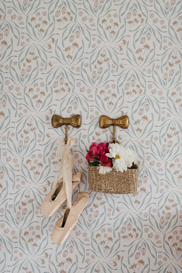 a basket with flowers on the wall next to two brass hooks and a pair of shoes