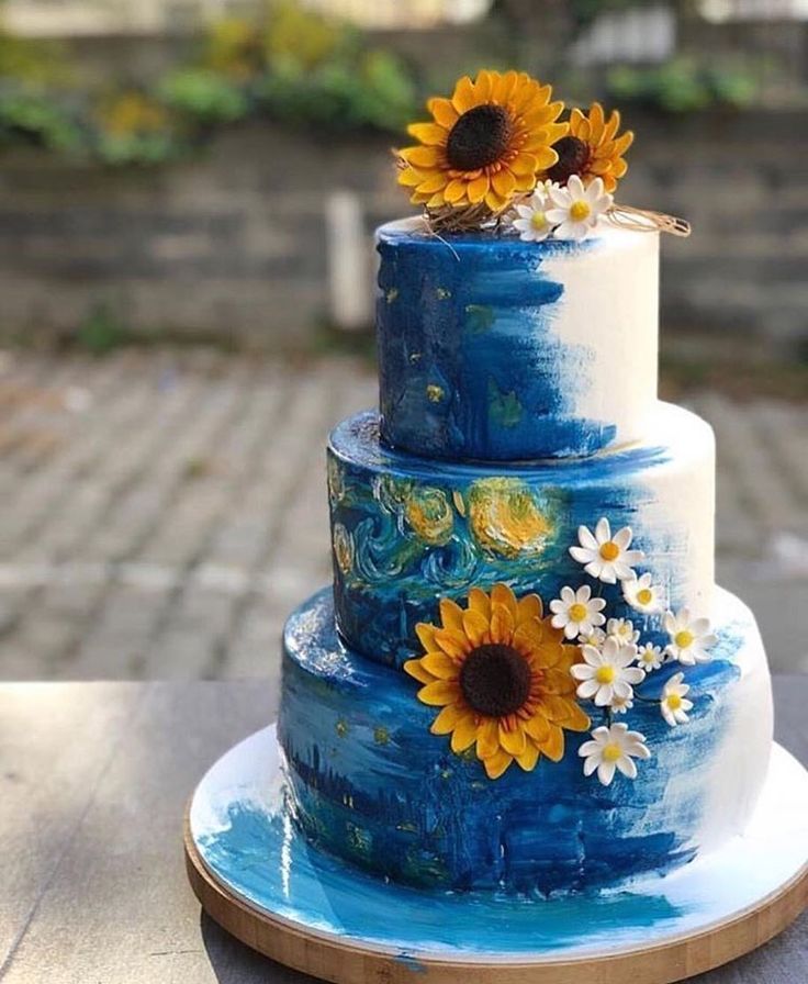 a three tiered blue cake with sunflowers on the top is sitting on a table