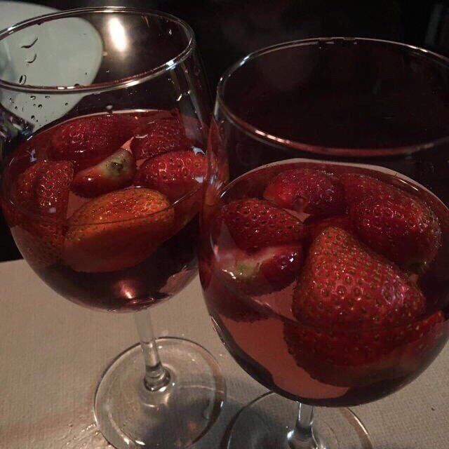 two wine glasses filled with red liquid and strawberries on the table next to each other