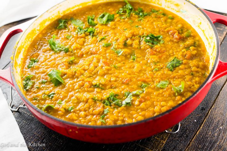 a red pot filled with lentils and cilantro on top of a wooden table