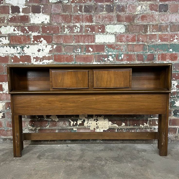 an old wooden bed frame with two drawers on the top and bottom, against a brick wall