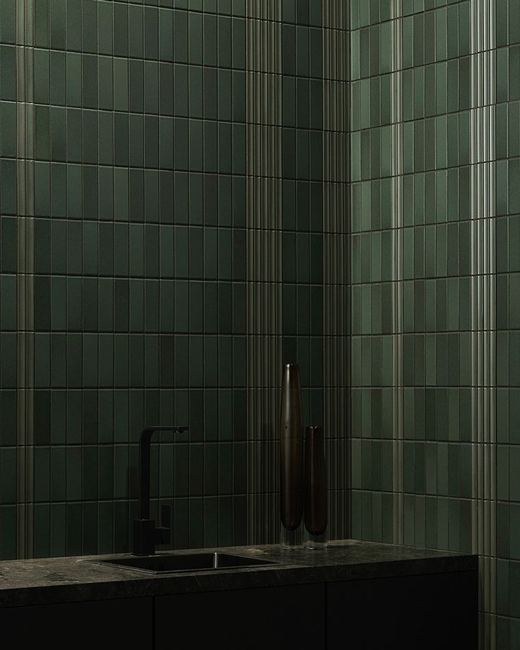 a bathroom with green tiled walls and a black sink in the corner next to it