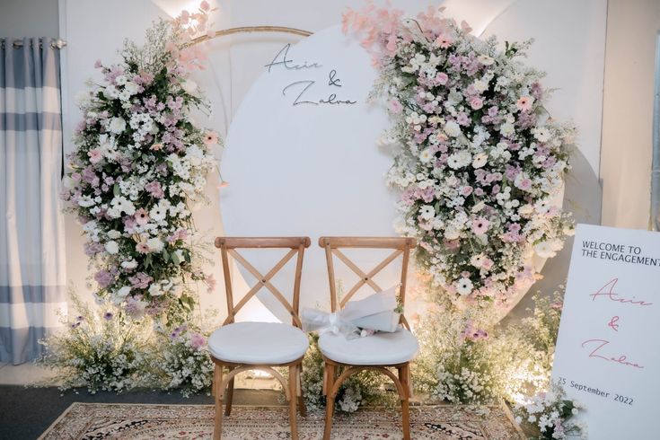 two wooden chairs sitting on top of a rug covered in flowers and greenery next to a white sign