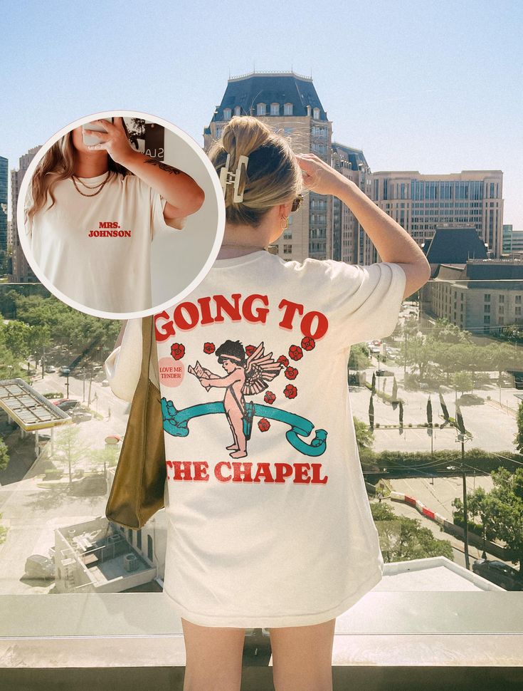 a woman standing on top of a building next to a cityscape and wearing a t - shirt that says going to the chapel