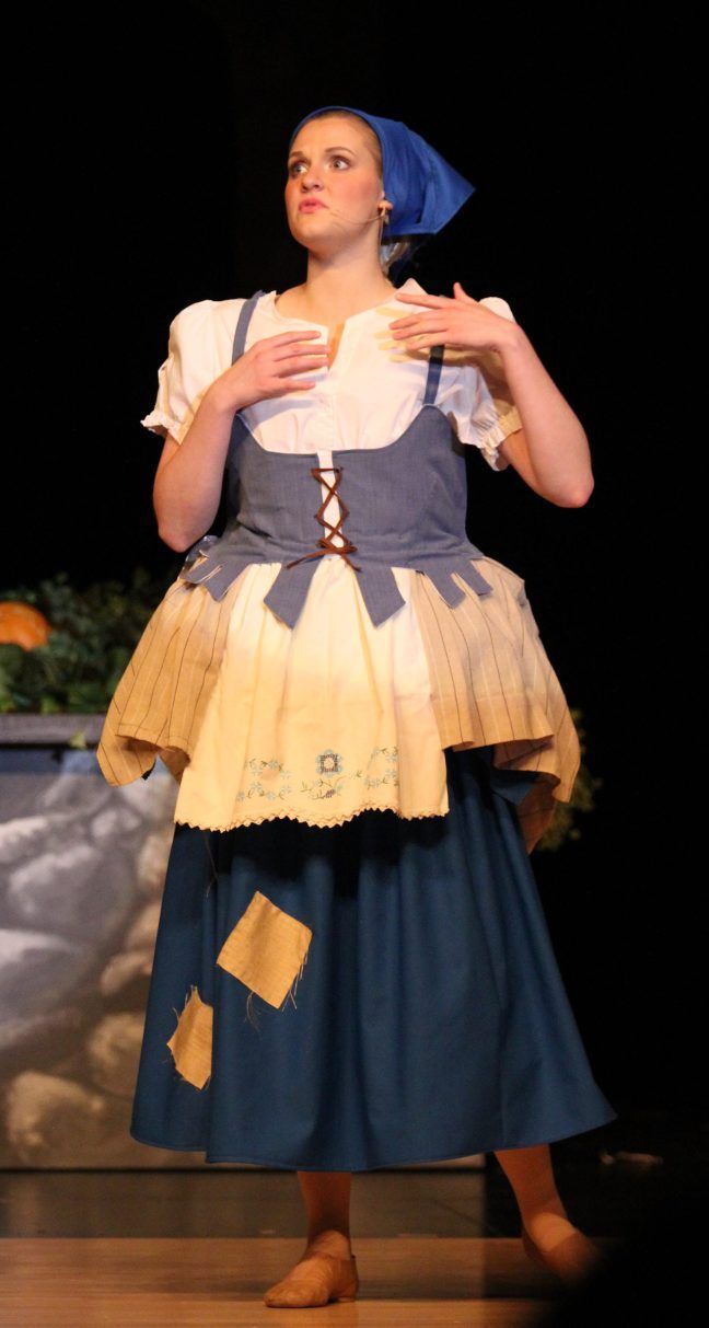 a woman in a dress standing on a stage with her hands out to the side