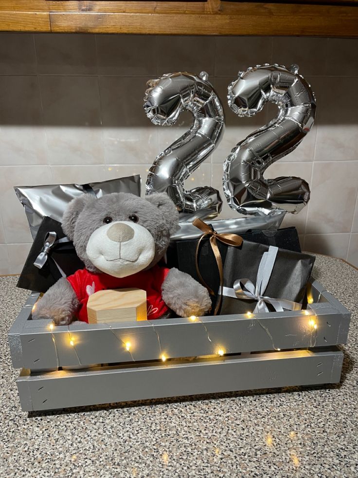 a teddy bear in a crate with balloons and gifts