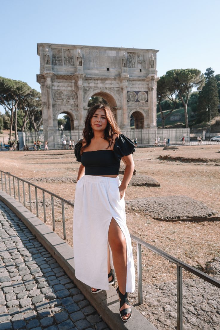 a woman standing in front of an arch of triumph wearing a white skirt and black top