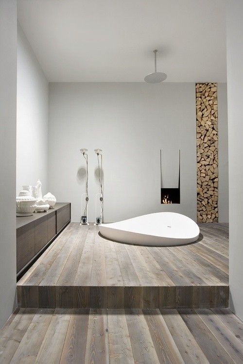 a white bath tub sitting on top of a wooden floor next to a fire place