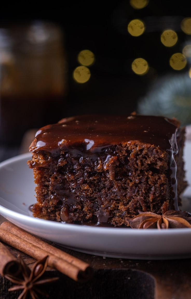 a piece of chocolate cake on a white plate with cinnamon sticks and anisette