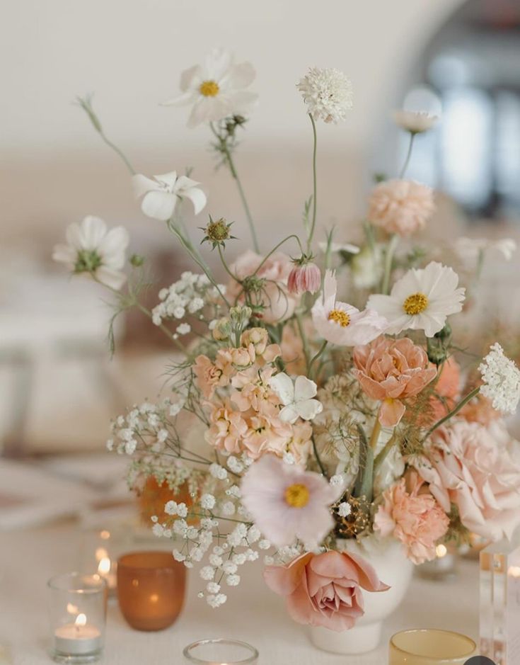 a vase filled with lots of flowers sitting on top of a table next to candles