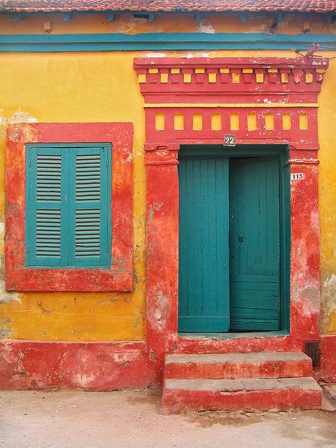 a red and yellow building with blue shutters on the front, and steps leading up to it