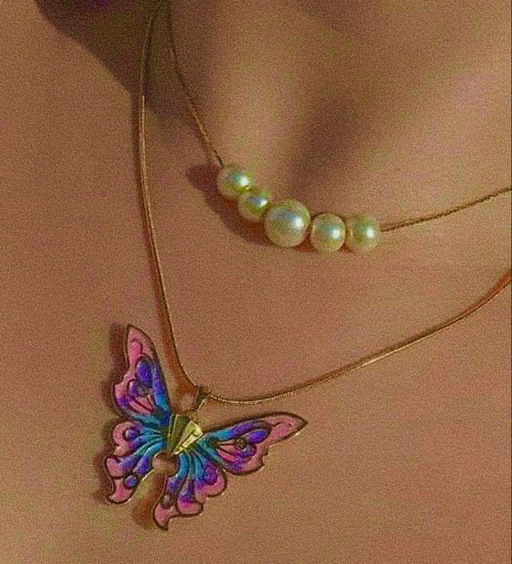 a necklace with a butterfly on it and pearls hanging from the back of it's neck